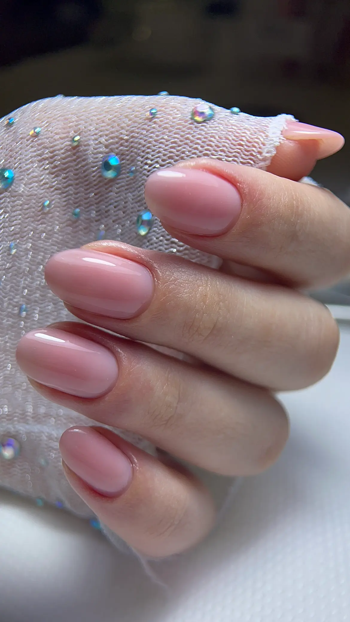 Pink almond manicure photographed against sparkling fabric